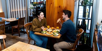 A dining area with wooden furniture, a table with plates of food, and a wine rack in the background.