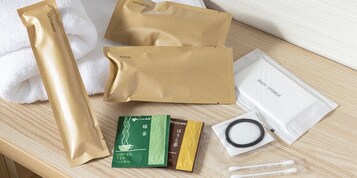 A wooden surface with various toiletries including a hair brush, razor, body sponge, green tea tea bags, and cotton swabs.