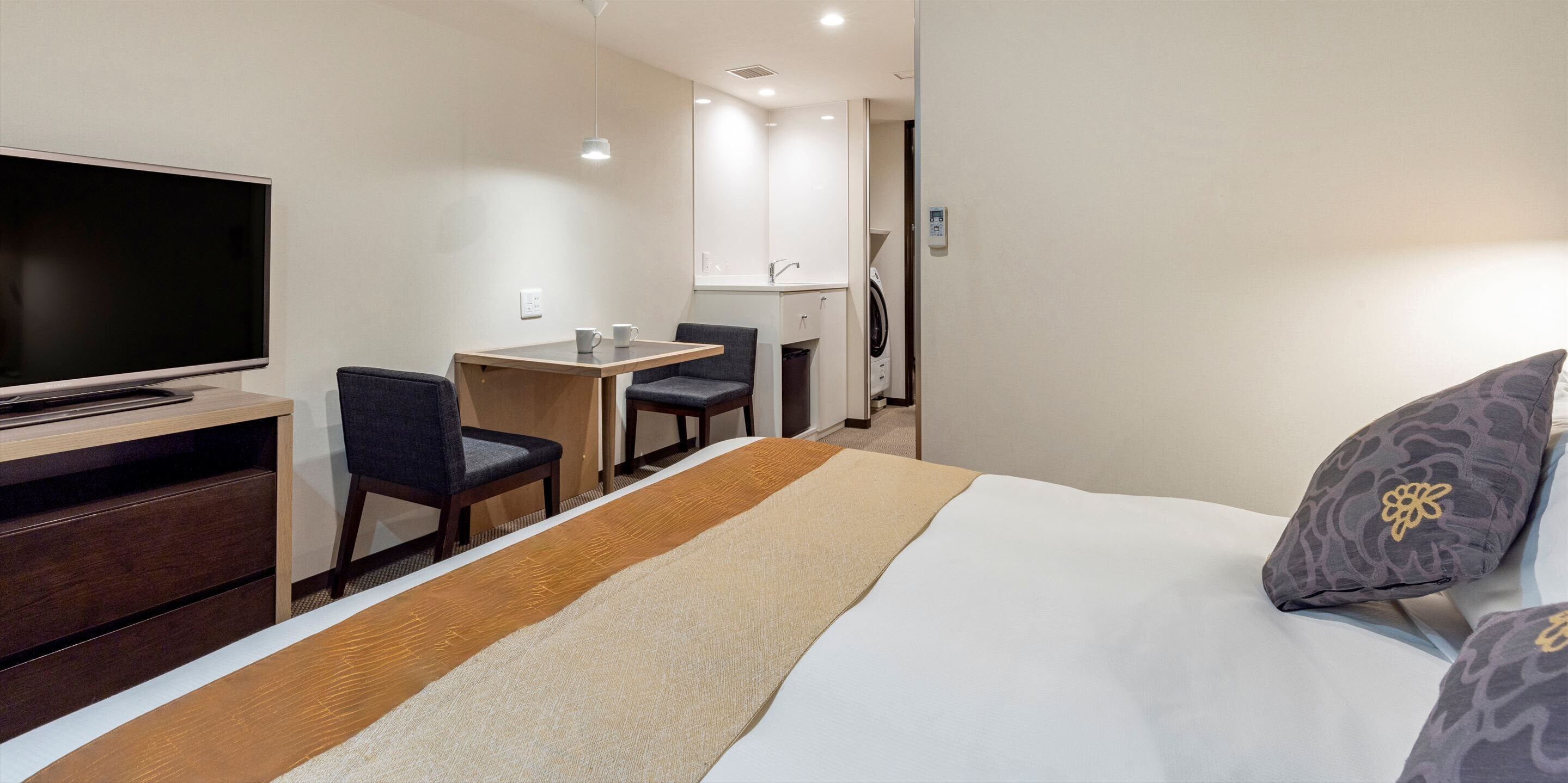 A hotel room with a bed, a desk, a chair, a TV, and a washing machine.