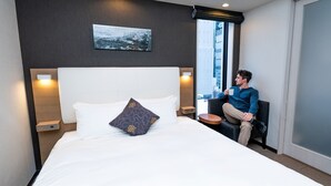 A hotel room with a large bed, a pillow, a bedside table, a chair, a window, and a wall-mounted picture. - Tokyu Stay Shimbashi (Ginza area) (Tokyo)