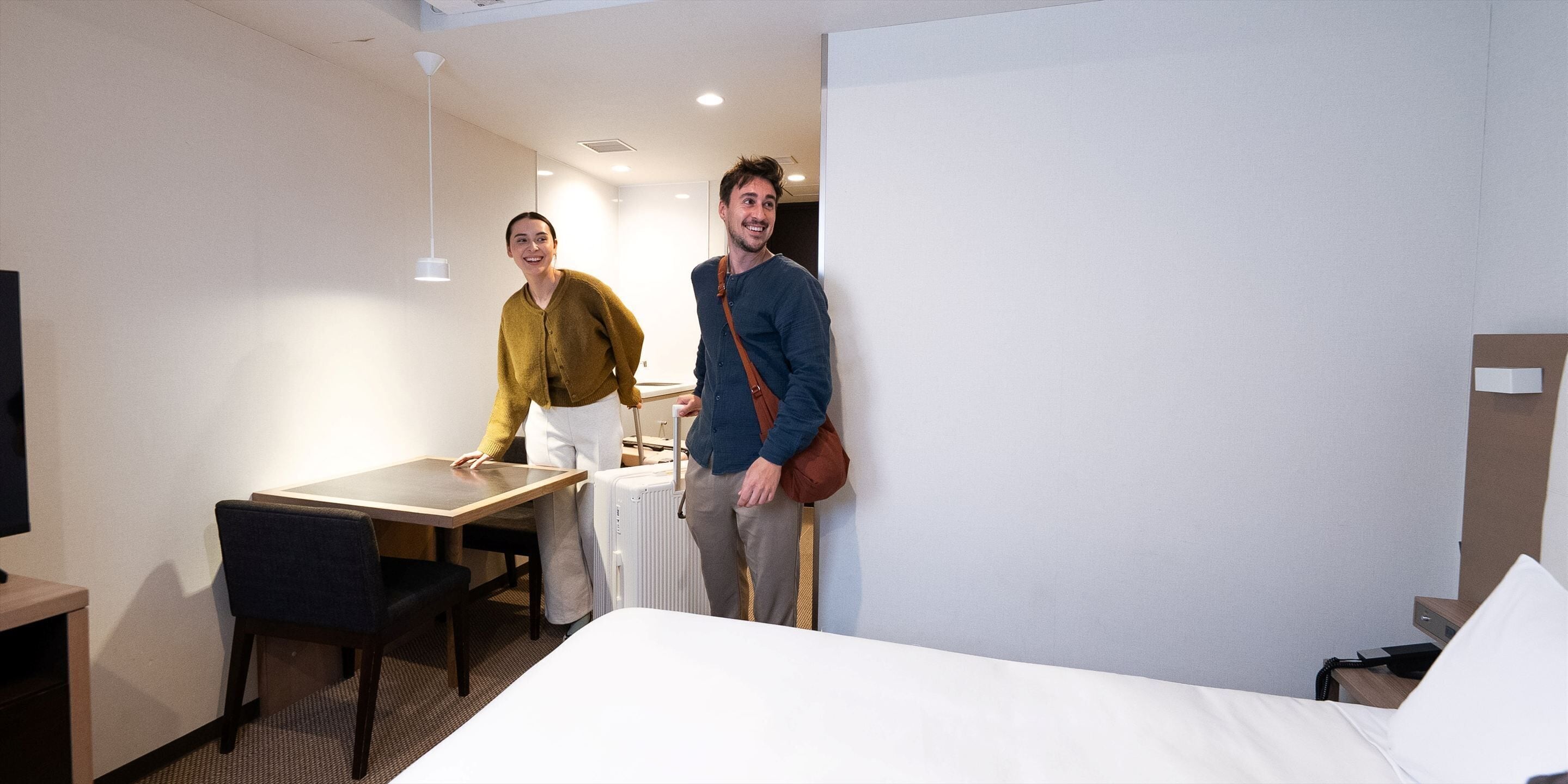 Une chambre d’hôtel avec un lit, un bureau, une chaise, une table et une valise.