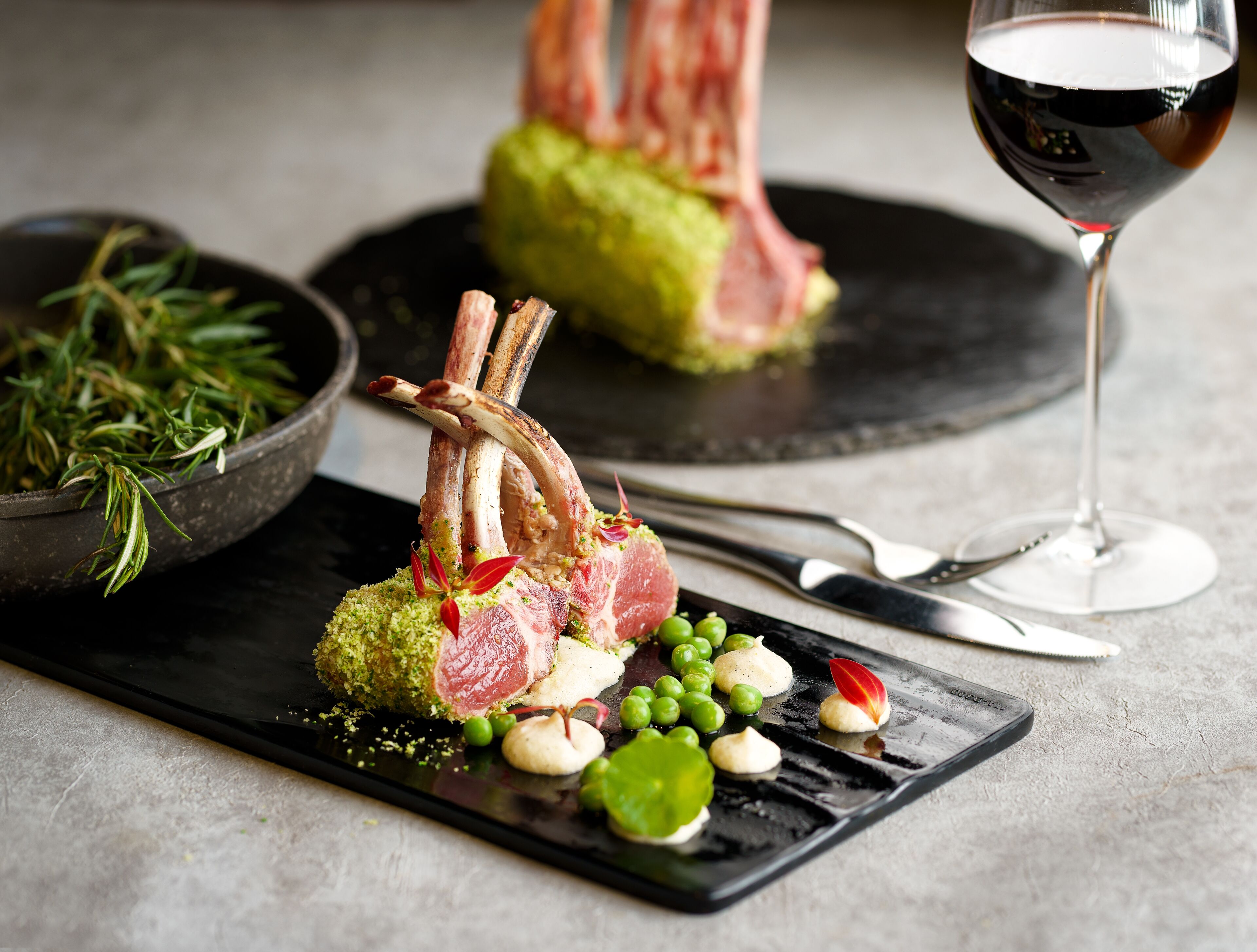 A plated dish with lamb chops, peas, and a wine glass.