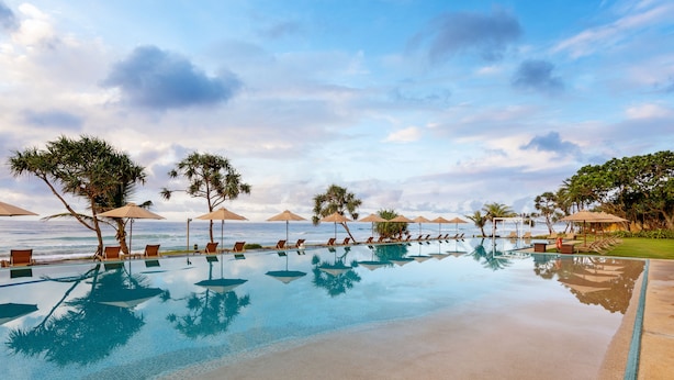 A poolside area with lounge chairs and umbrellas, a clear view of the ocean, and a tiled pool edge. - The Fortress Resort & Spa Galle (Koggala)
