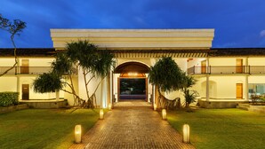 A building with a central entrance, surrounded by a paved pathway and palm trees. - The Fortress Resort & Spa Galle (Koggala)