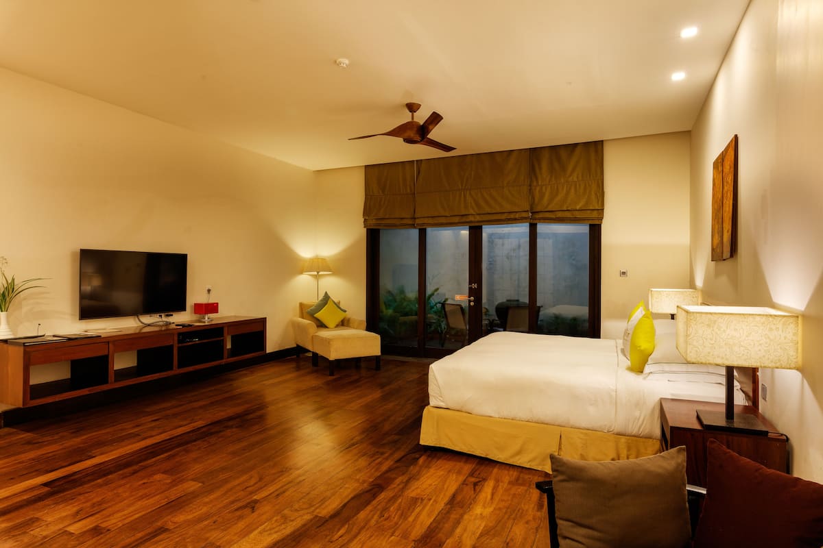 A modern hotel room with a large bed, a flat-screen TV, a ceiling fan, and a large window with a view of the outdoors.