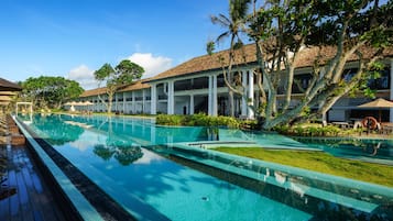 A resort pool area with clear blue water, wooden deck, and white buildings with balconies.