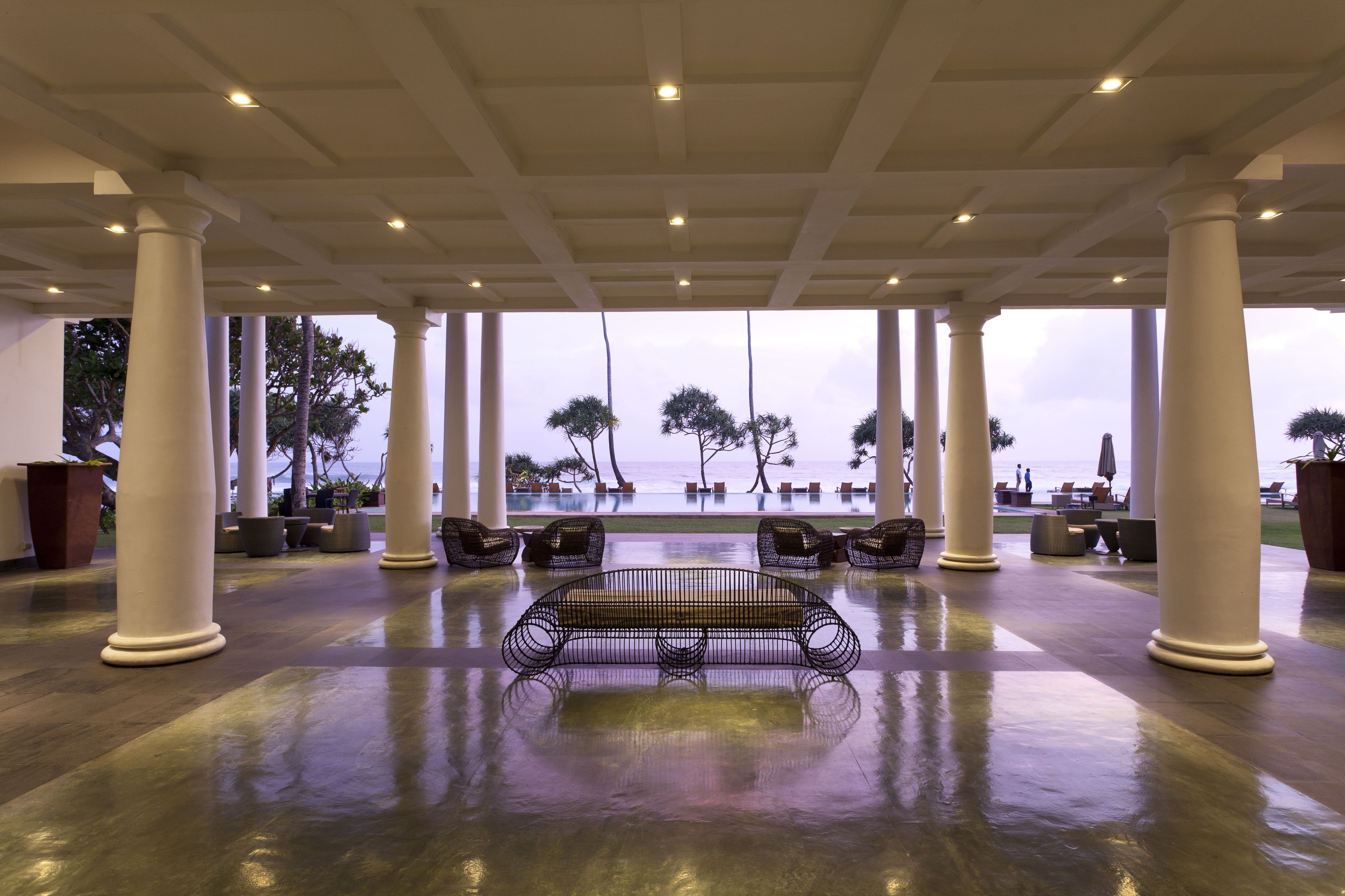 A spacious lobby with a wet floor, large white columns, and a bench in the center.