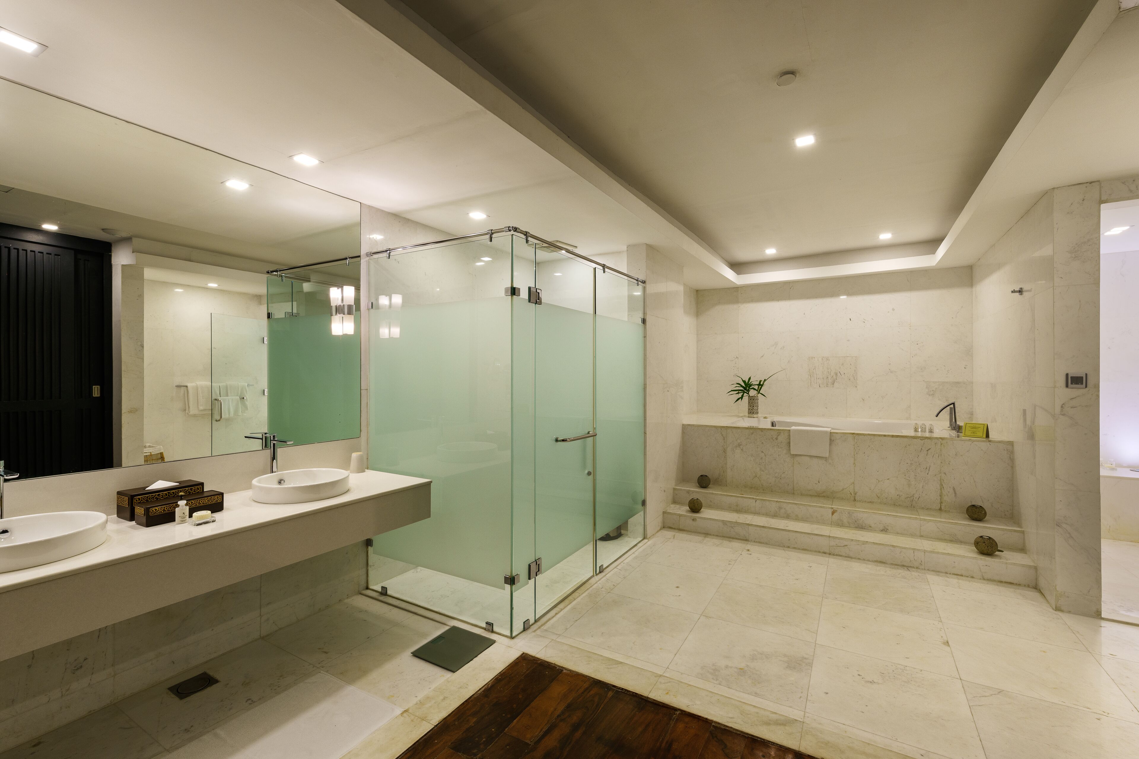 A modern bathroom with two sinks, a glass shower enclosure, a bathtub, and a large mirror.