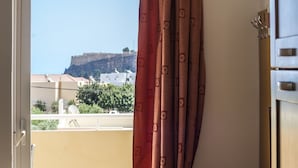A room with a view of a fort on a hill, a balcony with a railing, and a desk with a chair. - Lindos Blue Sky (Rhodes)