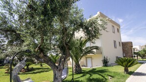 A residential building with a garden featuring a hanging chair, a palm tree, and a small bench. - Lindos Blue Sky (Rhodes)