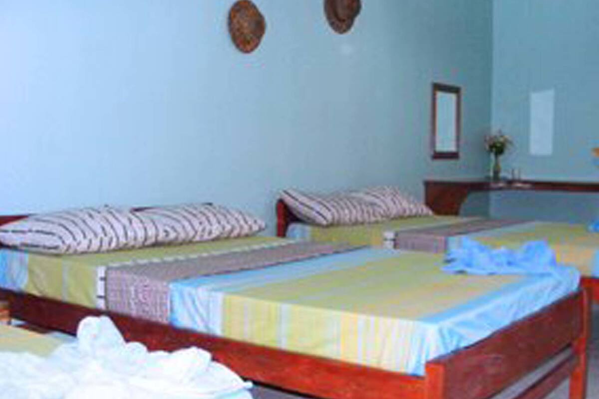 Ein Hotelzimmer mit zwei Einzelbetten, jeweils mit einem gestreiften Kopfkissen und einer farbenfrohen Tagesdecke. Es gibt einen kleinen Tisch mit einer Blumenvase und einen Spiegel an der Wand.