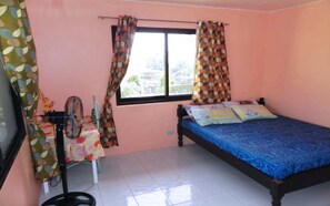 A bedroom with a bed, a window with curtains, a fan, and a table with a floral tablecloth. - Boracay Actopia Resort (Boracay Island)