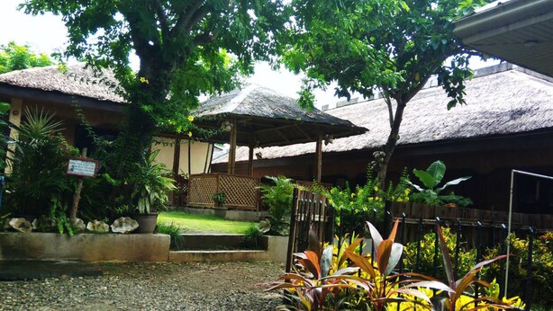 A courtyard with thatched-roof structures, a wooden fence, and tropical plants. - Boracay Actopia Resort (Boracay Island)