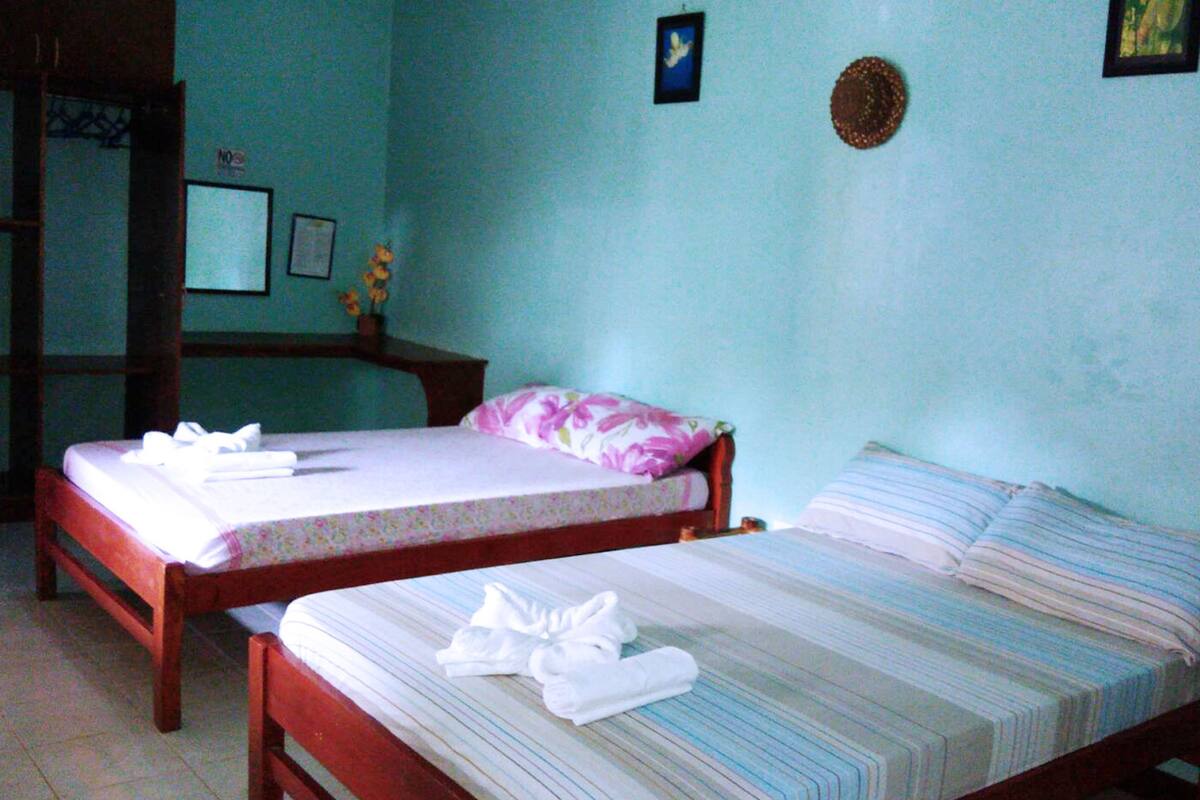 Ein Zimmer mit zwei Holzbett, jedes mit einem Kissen und einem ordentlich gefalteten weißen Handtuch.