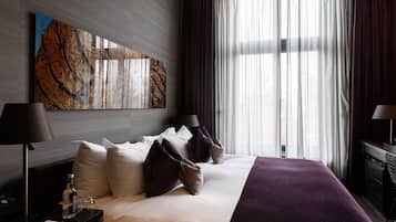 A modern hotel room with a large bed, a nightstand, a lamp, and a large window with curtains.