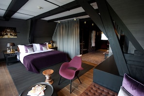 A modern hotel room with a large bed, a purple chair, a small round table, and a view of the outside. - Canal House (Amsterdam)