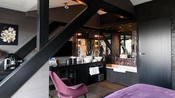 A modern bathroom with a large mirror, a sink, and a vanity. There is a staircase leading to another level.