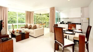 A modern living room with a sofa, coffee table, and dining area with chairs and a table set for a meal. - The Park Surin by RESAVA (Choeng Thale)