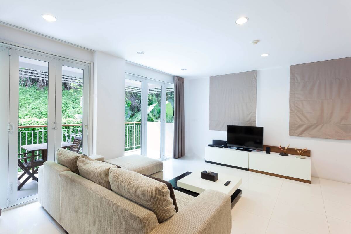 A modern living room with a sofa, coffee table, TV, and sliding glass doors leading to an outdoor patio.