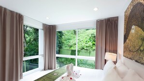 A hotel room with a large bed, a view of greenery through the windows, and a decorative wall piece. - The Park Surin by RESAVA (Choeng Thale)