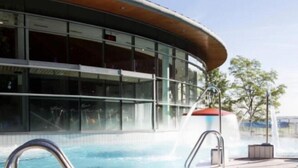 A swimming pool with clear water, a modern building with large windows, and a fountain.