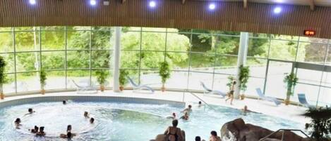 Una gran piscina interior con varias personas nadando y descansando.