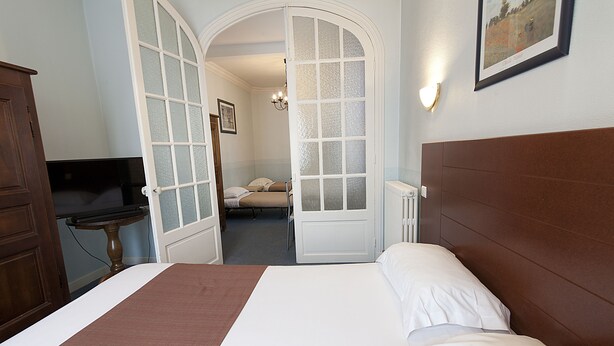 A hotel room with a bed, a desk, and an arched doorway leading to another room.