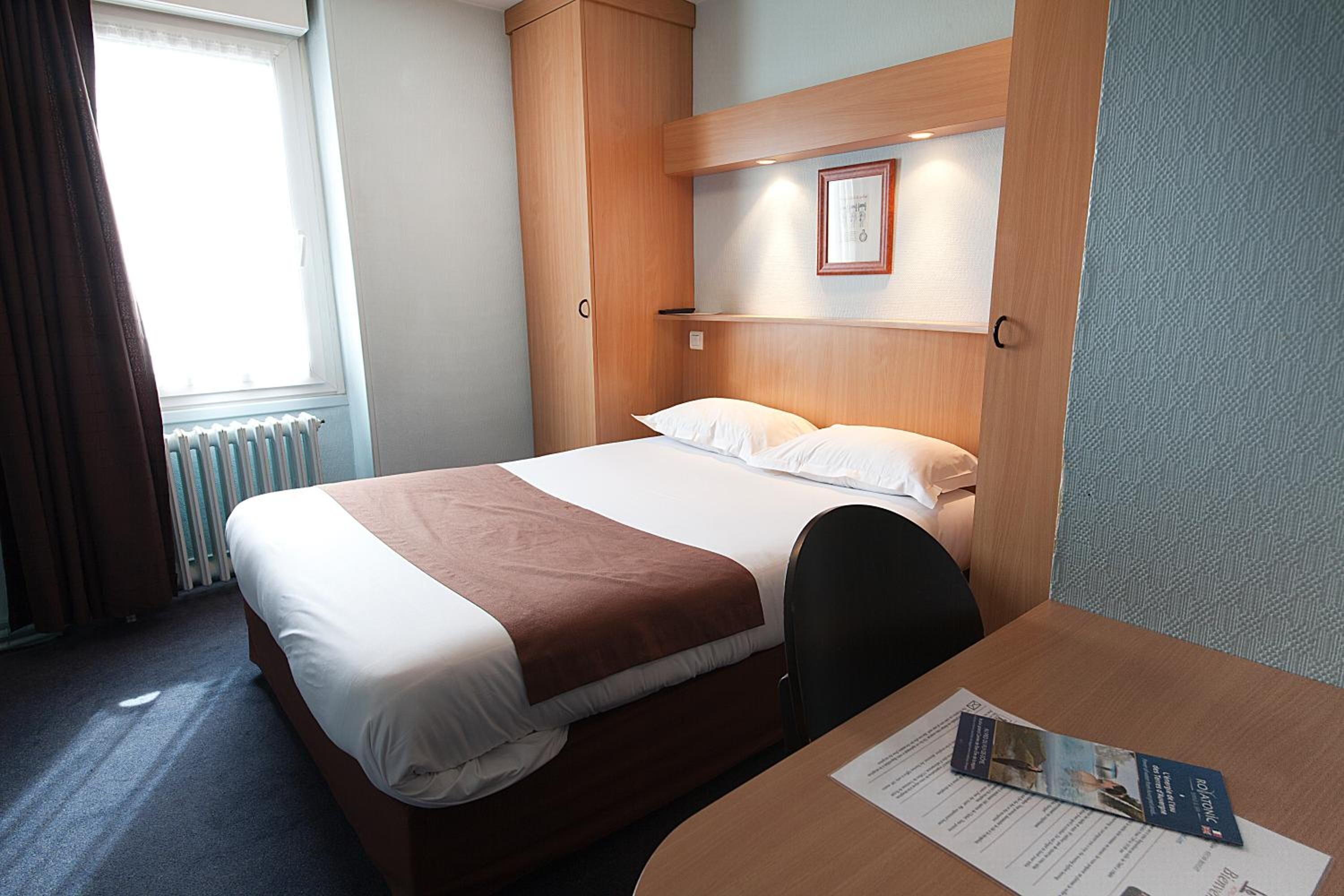 A hotel room with a bed, a desk, and a window with curtains.