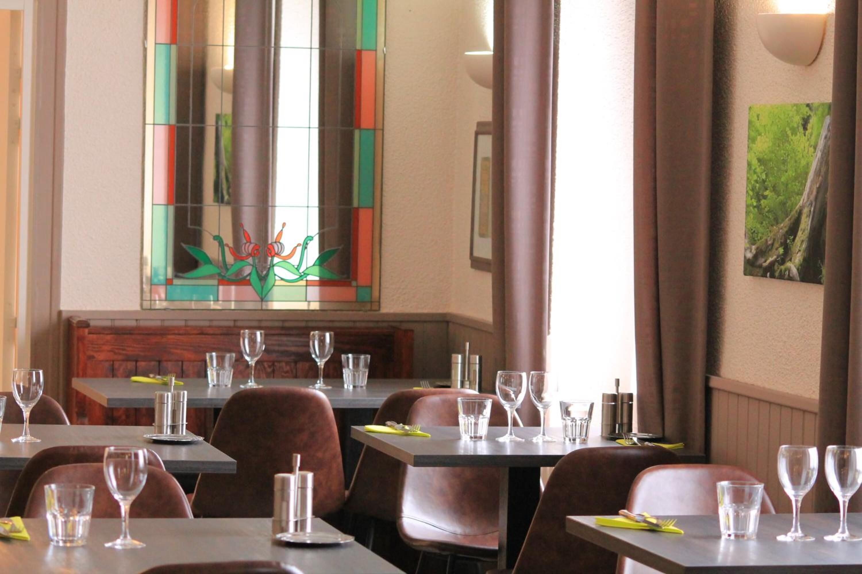 L’intérieur d’un restaurant, avec des tables dressées pour le service, un vitrail et un tableau encadré accroché au mur.