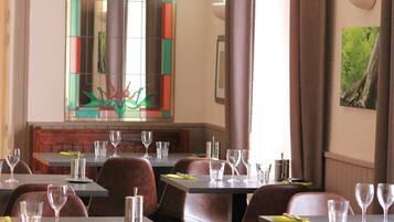 L’intérieur d’un restaurant, avec des tables dressées pour le service, un vitrail et un tableau encadré accroché au mur.