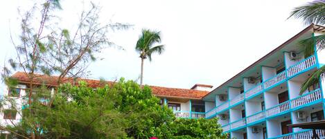 Un edificio de varios pisos con balcones, techo de tejas rojas y una palmera al fondo.
