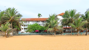 A beach with palm trees and a building with a red roof. - Topaz Beach Hotel (Negombo)