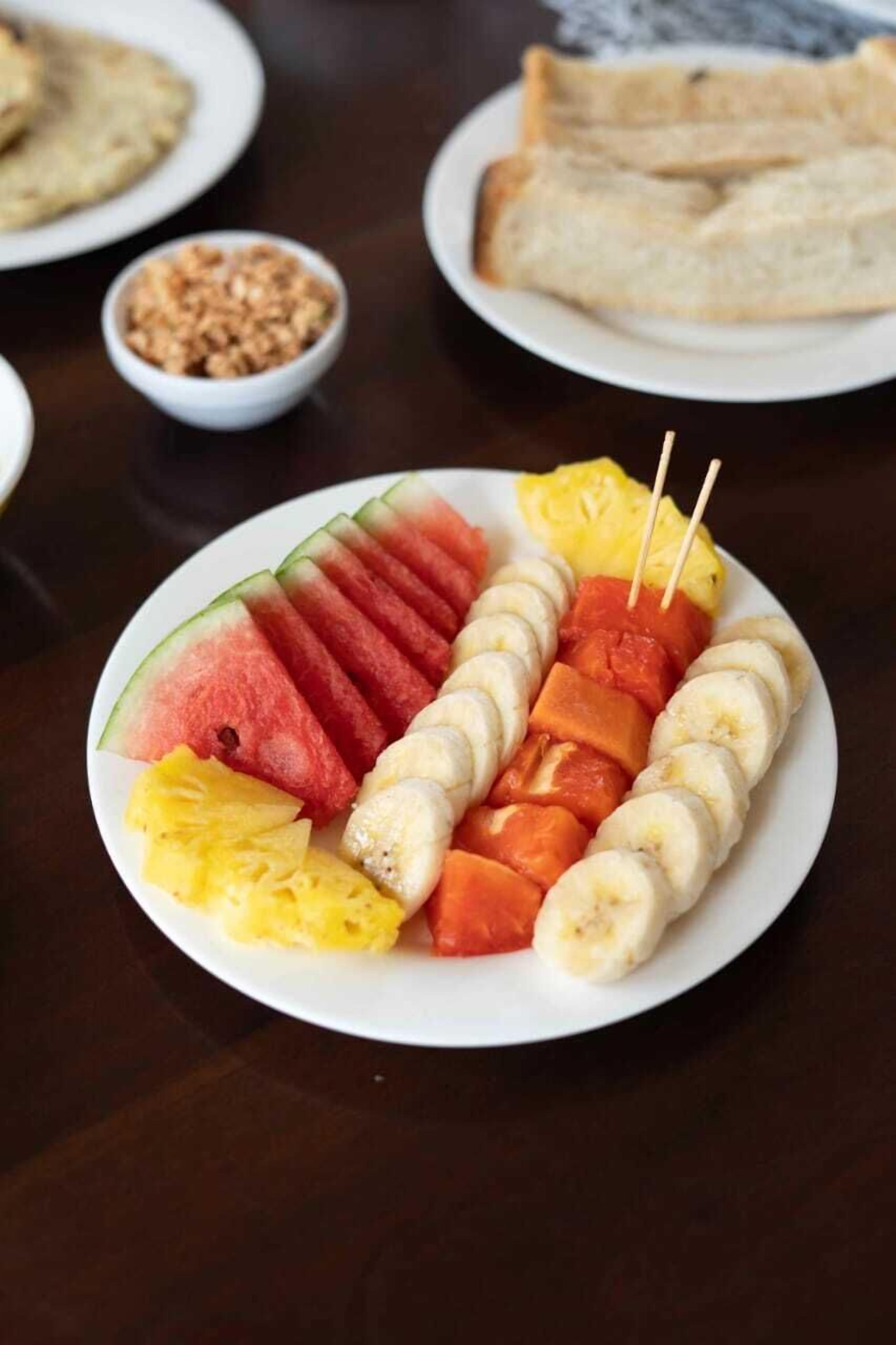 A plate with fruit skewers, a bowl of nuts, and a plate of bread.