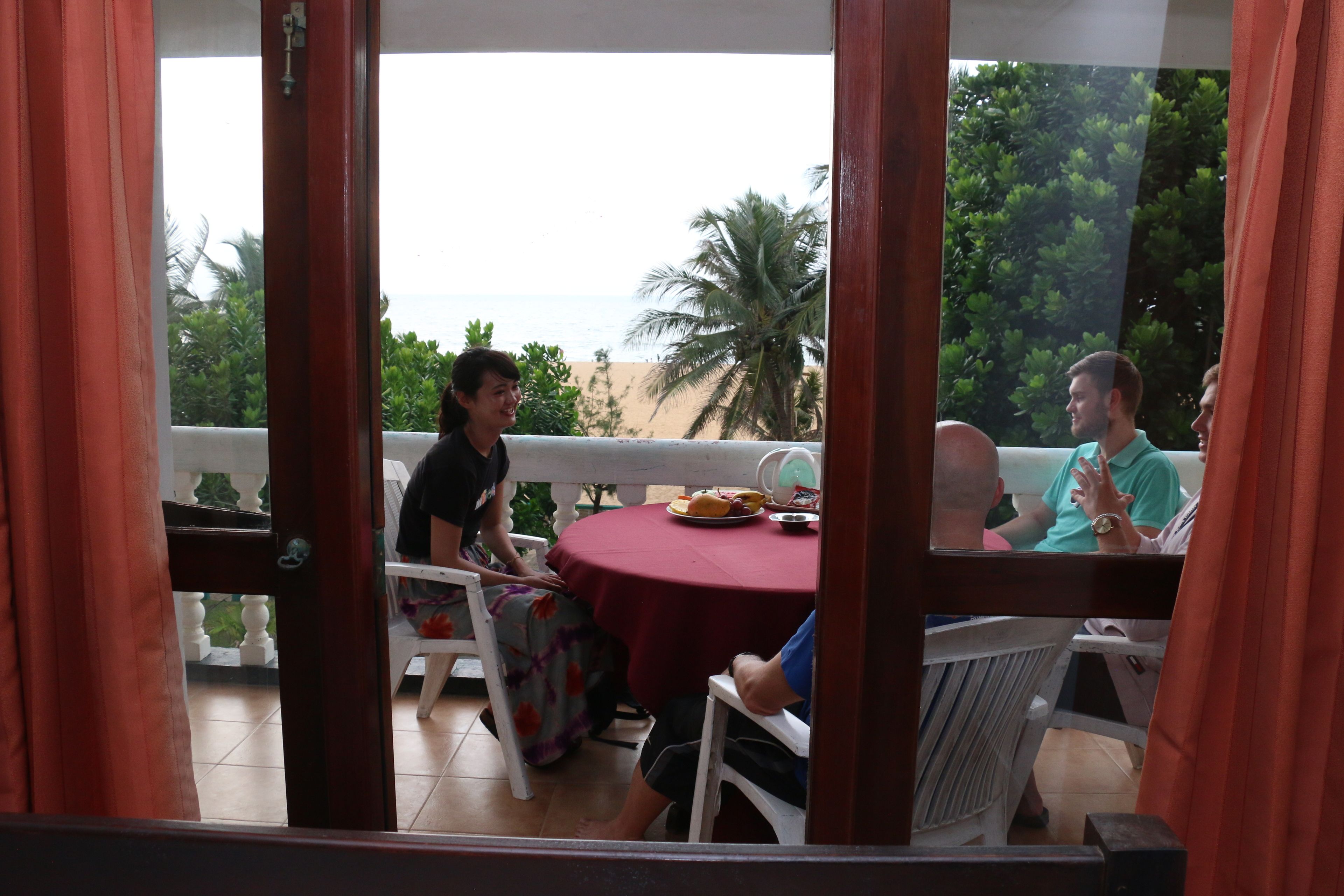 Un balcón con mesa y sillas, con vistas a una playa y palmeras.