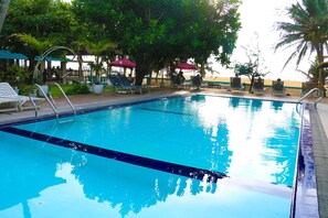 A clear blue swimming pool with lounge chairs and umbrellas, surrounded by trees and a view of the beach. - Topaz Beach Hotel (Negombo)