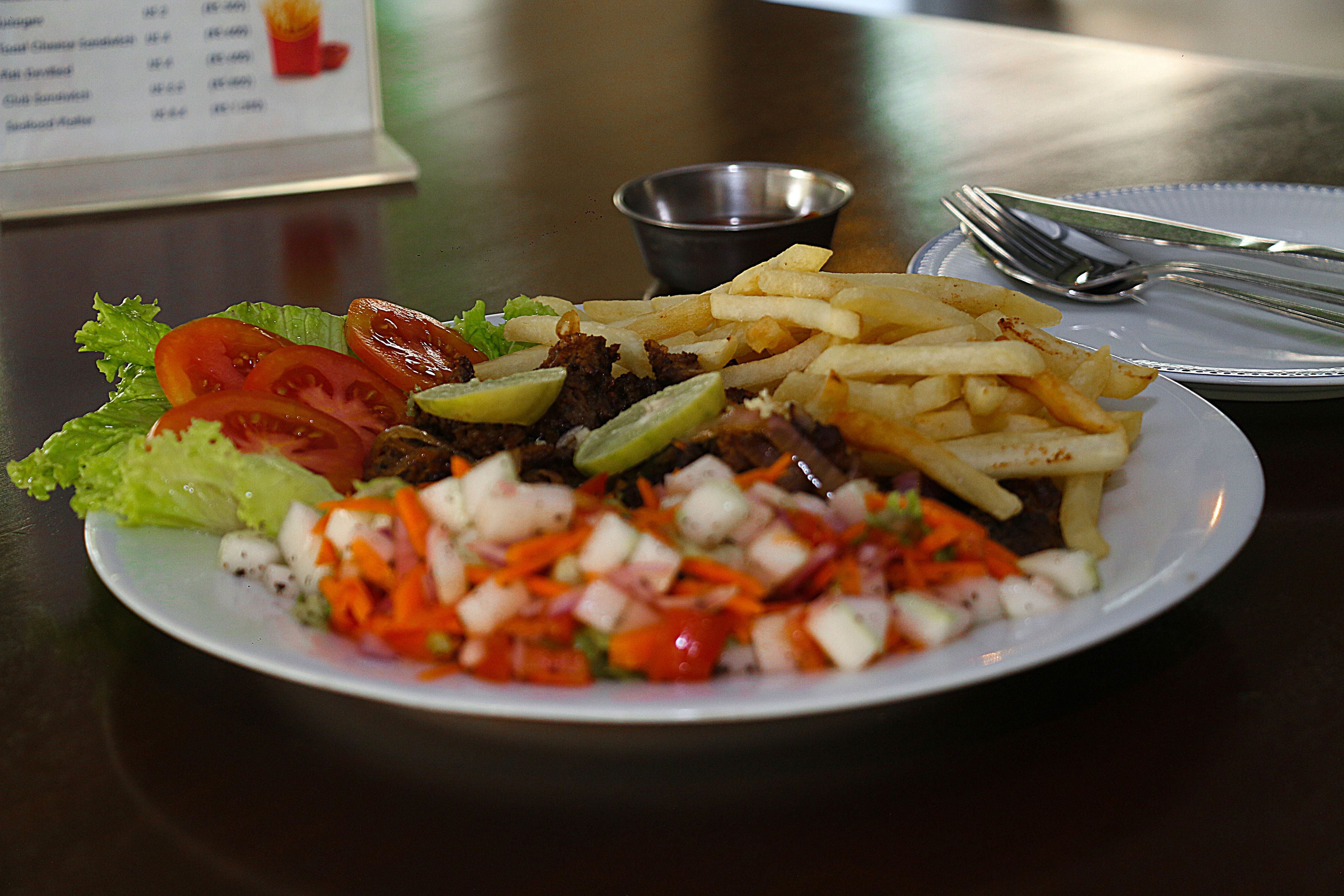 A plate of food with fries, salad, and meat, accompanied by a small bowl of sauce and cutlery on a table.