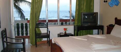 A bedroom with a bed, a chair, a small table with a TV, and a view of the ocean.