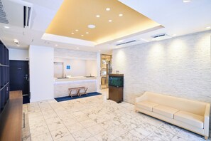 A hotel lobby with a reception desk, a sofa, a fish tank, and a marble floor.