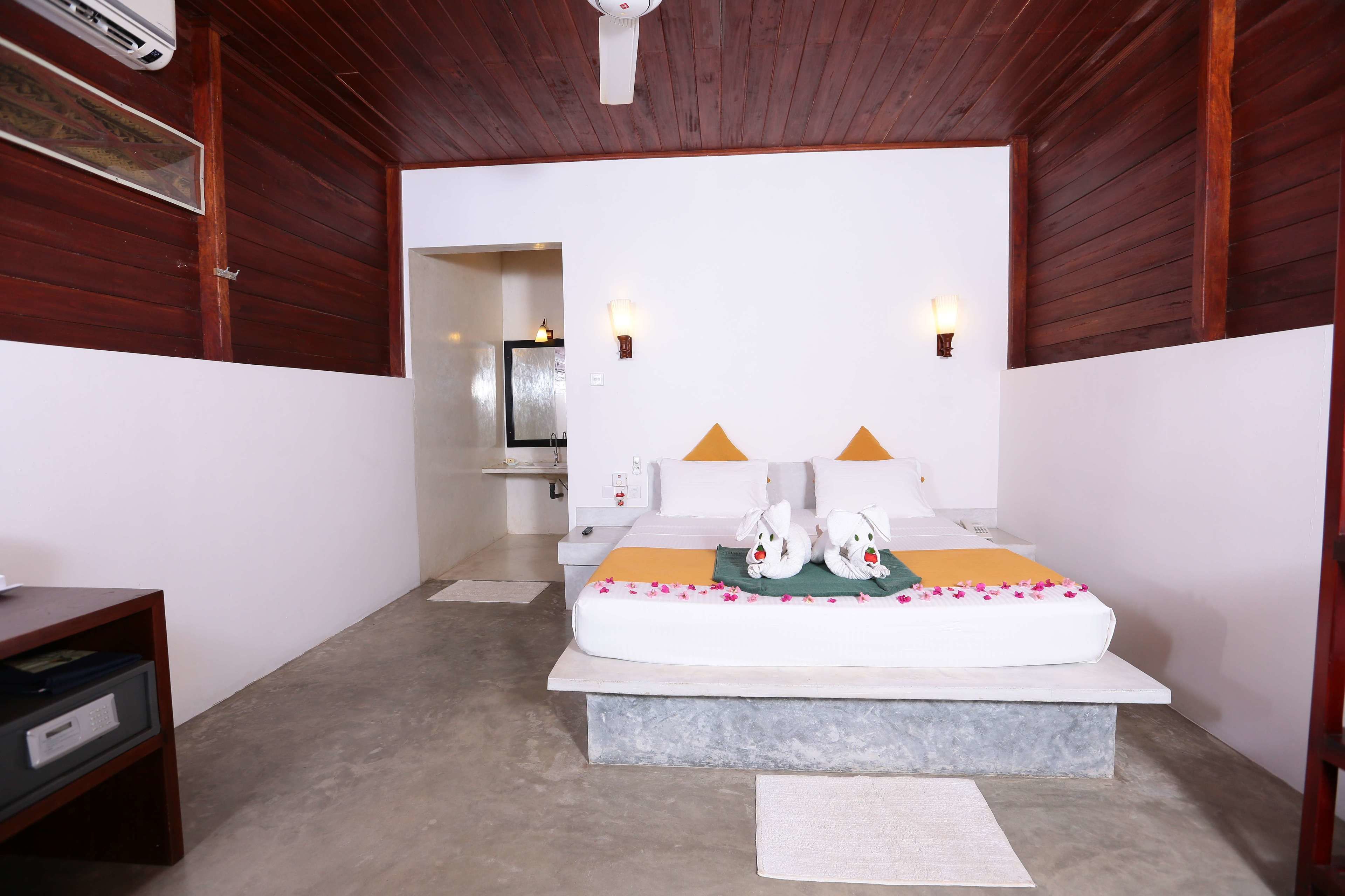 A bedroom with a bed, bedside lamps, a wooden ceiling, and a small desk.