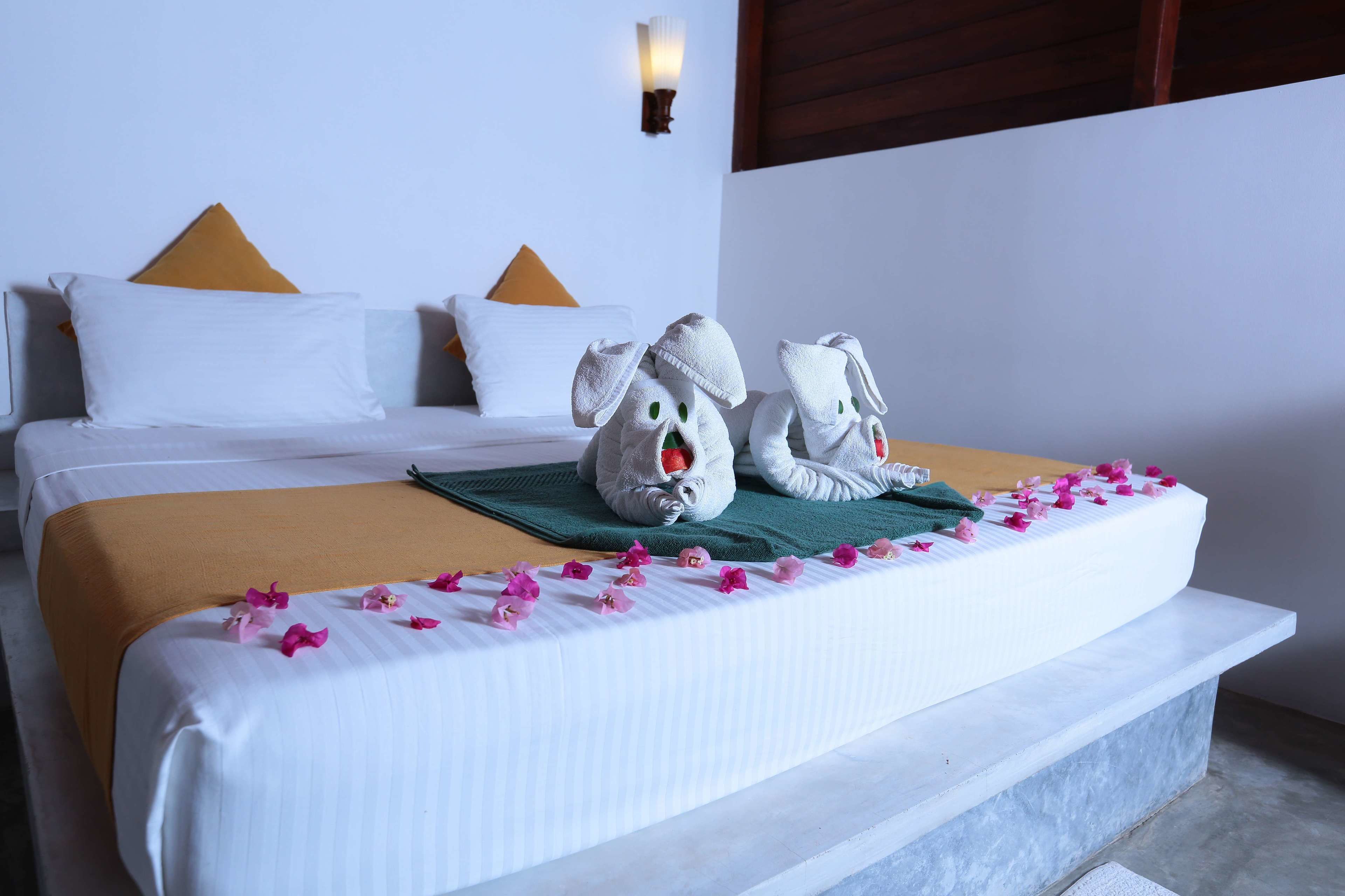 A neatly made bed with a white and orange bedspread, two towels shaped like animals, and pink flower petals on the bed.