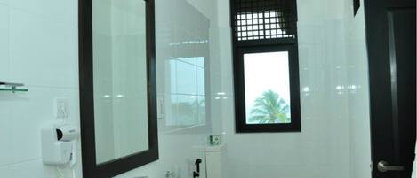 A modern bathroom with a large mirror, a sink, a toilet, and a window with a view of palm trees.