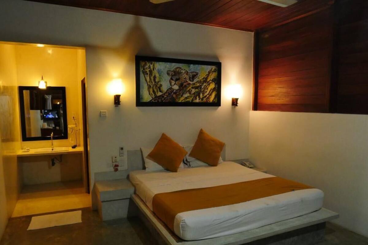 A bedroom with a bed, two pillows, a nightstand, a mirror, and a painting on the wall.