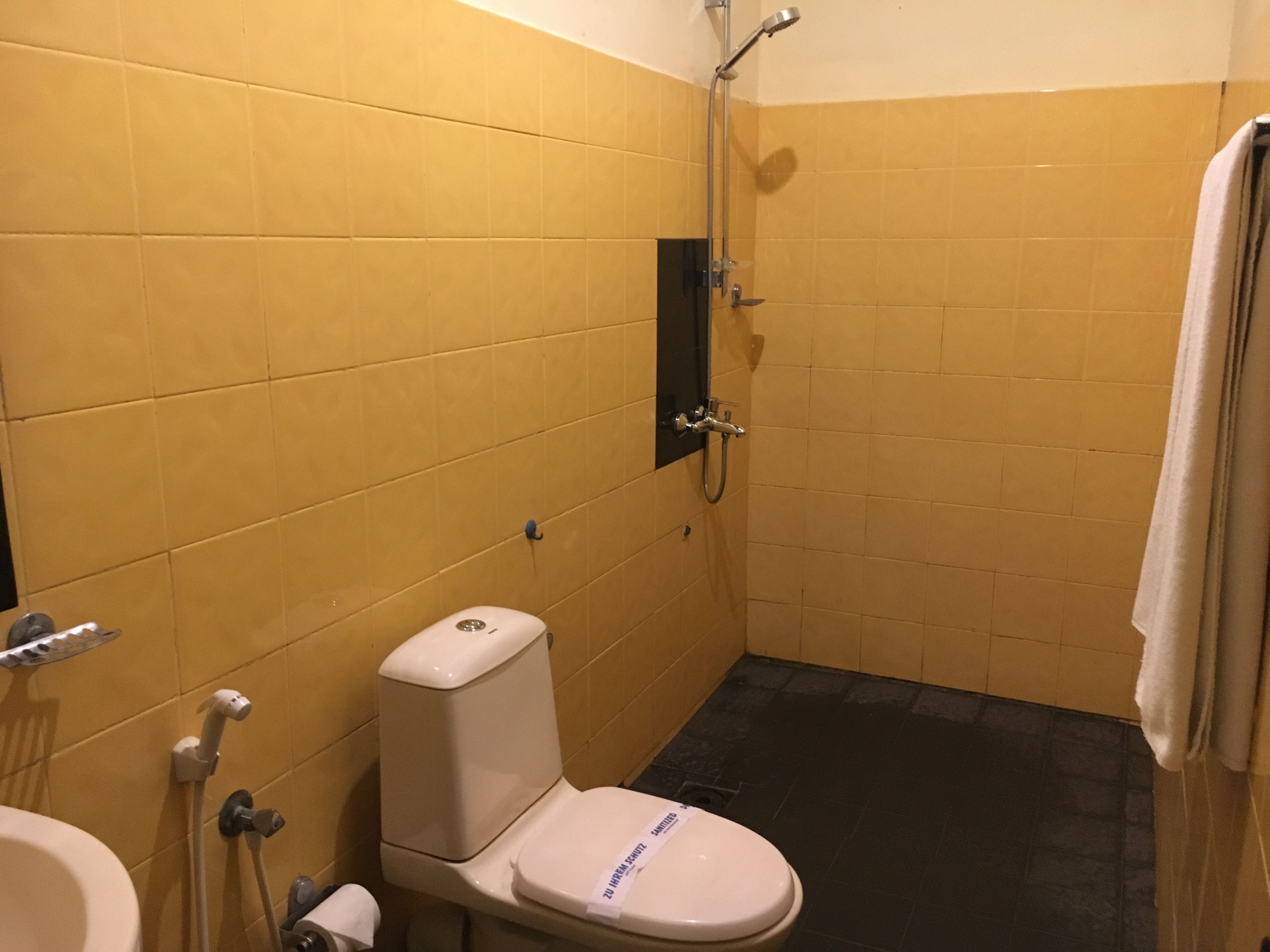 A small bathroom with yellow tiles, a white toilet, a black floor, and a shower area.