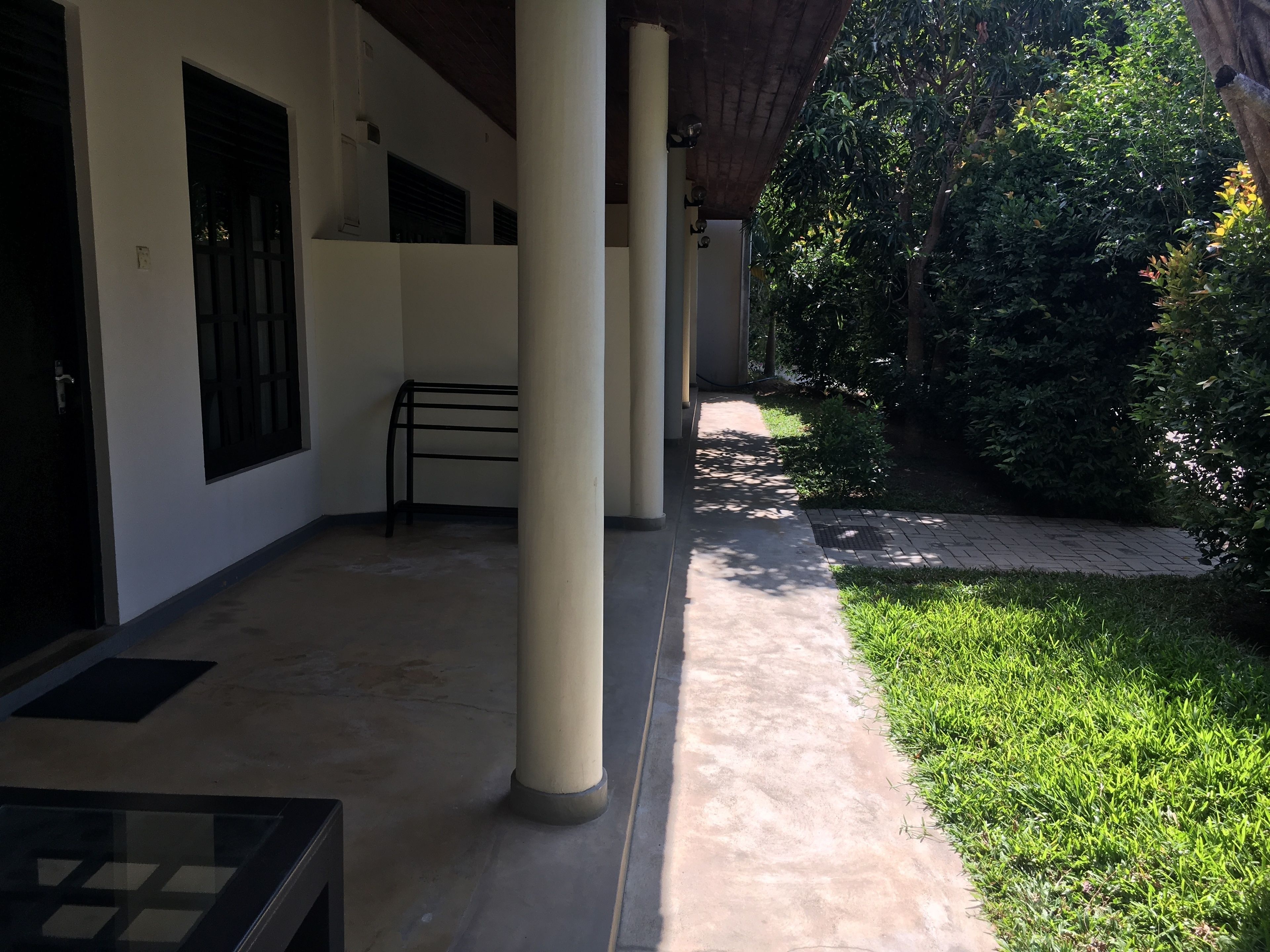 Un espacio al aire libre cubierto con columnas, un banco y un sendero que lleva a un jardín.