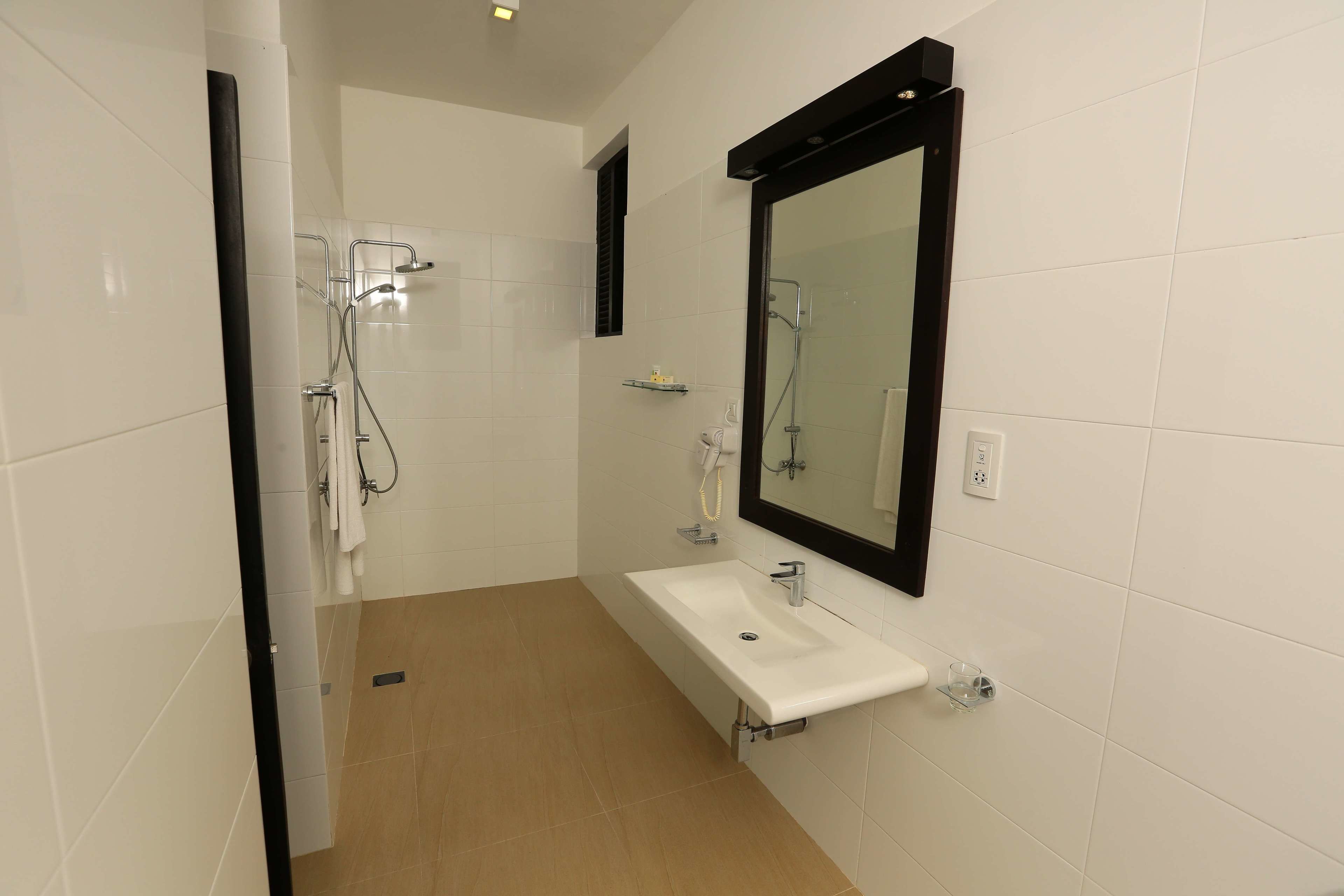Et moderne badeværelse med en hvid vask, et stort spejl og et bruseområde.