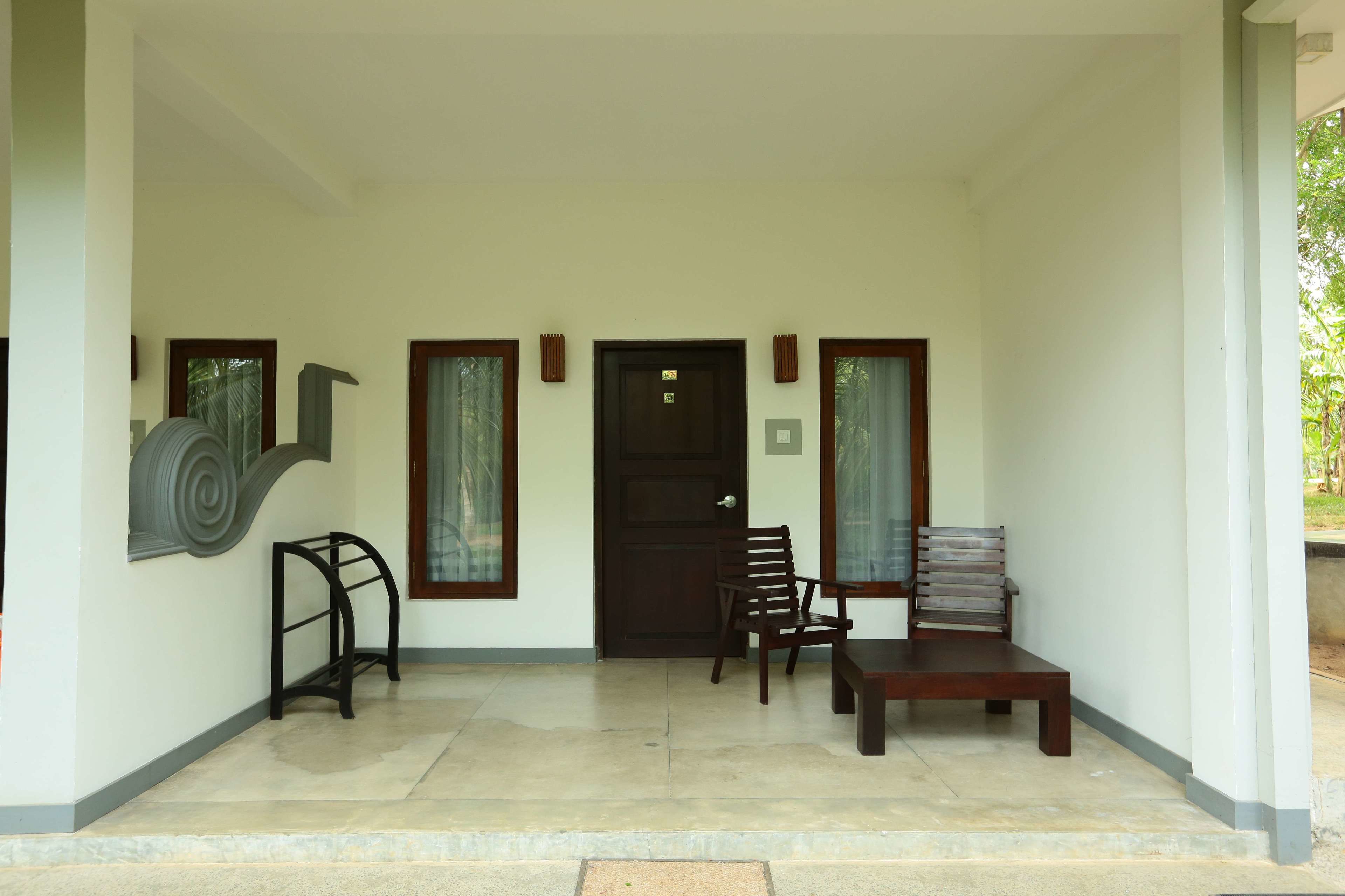 A clean, modern entrance with a dark wooden door, two wooden chairs, a bench, and a small table.