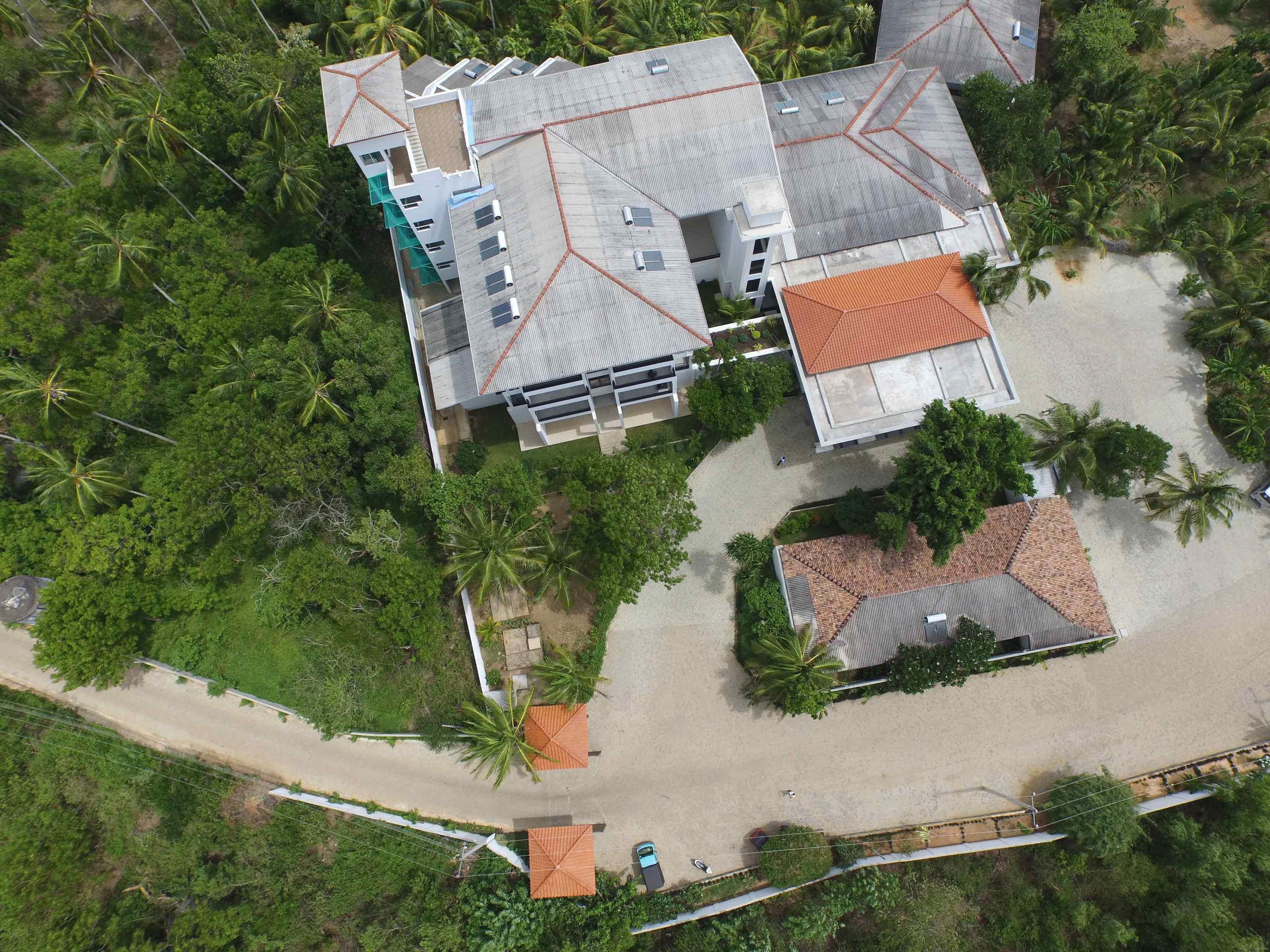 An aerial view of a residential complex with multiple buildings, surrounded by lush greenery and palm trees.