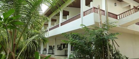 A multi-level building with a central courtyard surrounded by lush greenery, including palm trees and various plants.