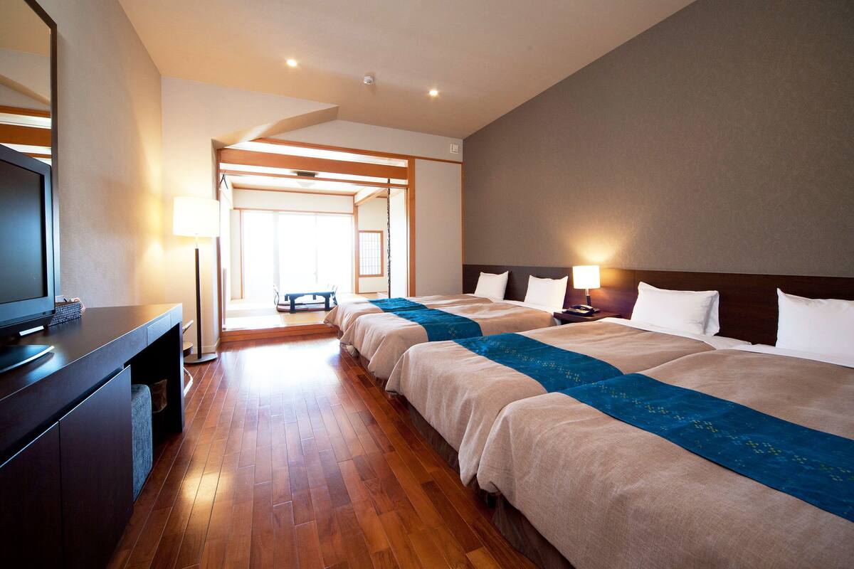 Habitación de hotel con dos camas, un escritorio con televisor y vistas a un interior japonés tradicional.