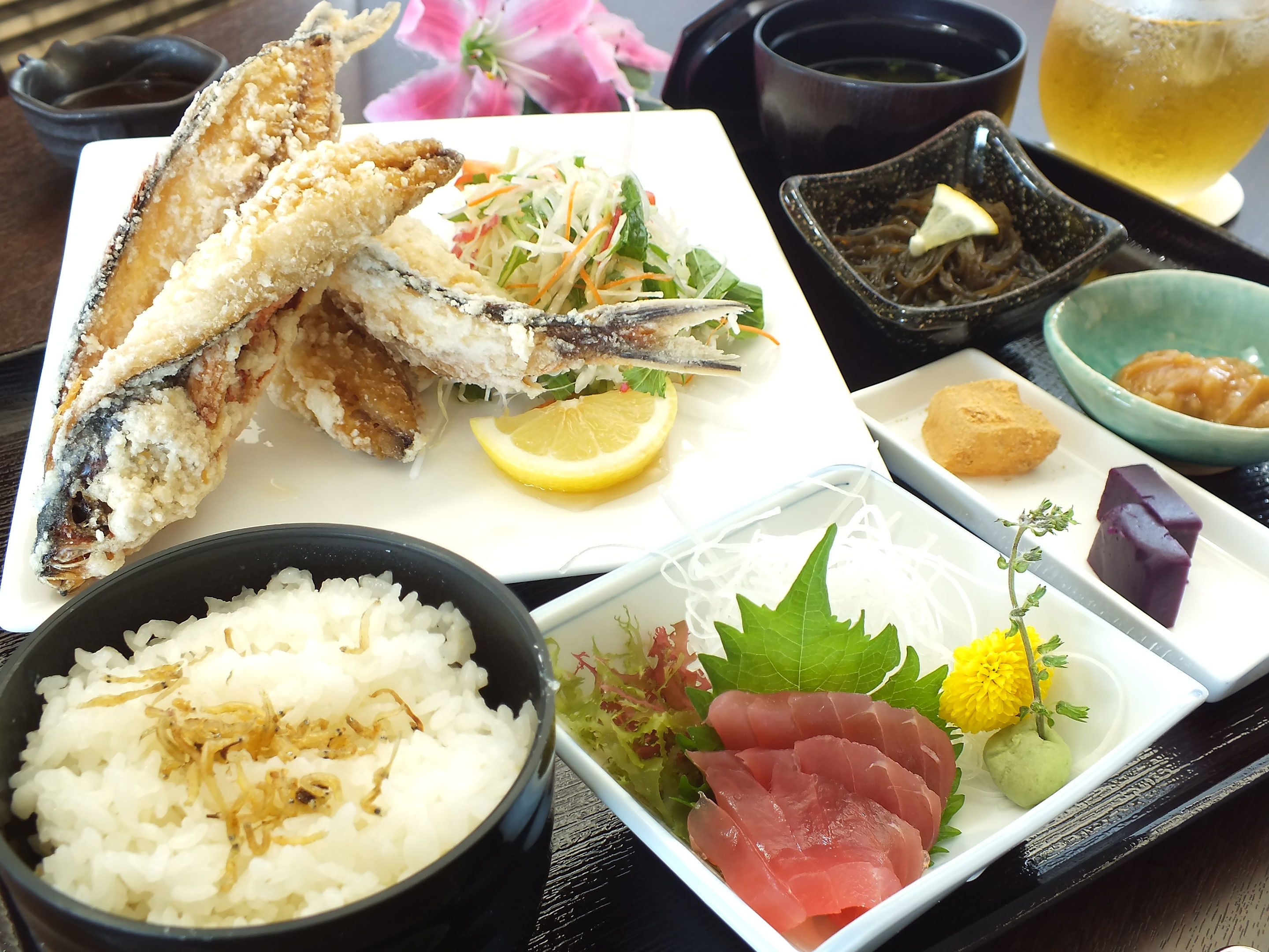 Diversos platos que incluyen pescado frito, arroz, sashimi y una ensalada con una rodaja de limón.
